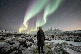 Voyageuse contemplant l'aurore boréale en Islande sur un champ de lave enneigé sous un ciel étoilé